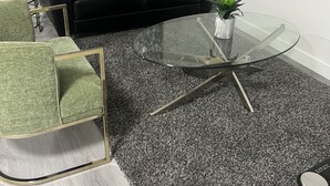 A modern living room with a black leather sofa, a glass coffee table, a green armchair, and a grey carpet. - New basement suite in Saskatoon's newest neighborhood. Welcome to the Casa! (Saskatoon)