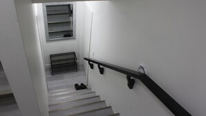 A staircase with a metal handrail, a window with a metal frame, and a shoe rack against the wall. - New basement suite in Saskatoon's newest neighborhood. Welcome to the Casa! (Saskatoon)