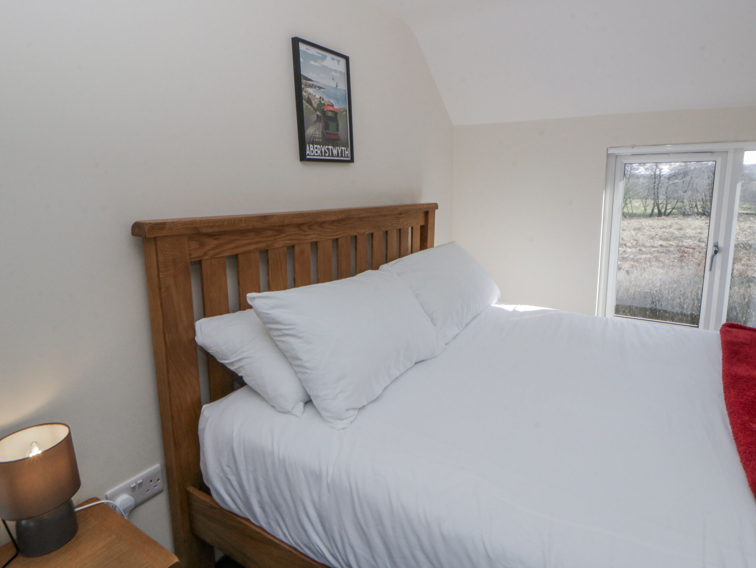 A bedroom with a wooden headboard, white bedding, a bedside lamp, and a framed picture on the wall.