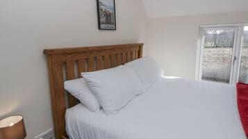 A bedroom with a wooden headboard, white bedding, a bedside lamp, and a framed picture on the wall.