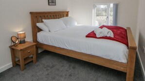 A neatly made bed with white linens and a red blanket, a bedside table with a lamp, and a window with curtains. - Glandwr House (Llandrindod Wells)