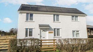 A two-story house with a white exterior, solar panels on the roof, and a wooden fence in front. - Glandwr House (Llandrindod Wells)