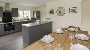 A modern kitchen with grey cabinets, a central island, and a dining area set for six with white plates and glasses. - Glandwr House (Llandrindod Wells)