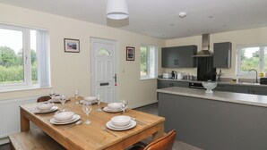 A modern kitchen with grey cabinets, a wooden dining table set for four, and a view of greenery outside. - Glandwr House (Llandrindod Wells)