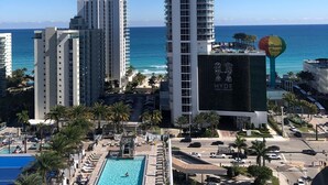 Un hotel de gran altura con piscina en la azotea y vistas al océano, con un letrero que dice Hallandale Beach.