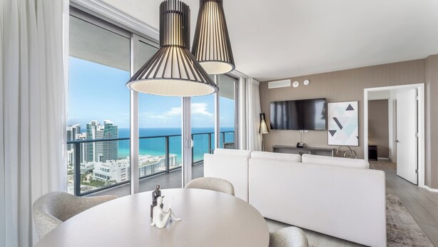Una sala de estar moderna con un sofá blanco, una mesa de comedor redonda y vista al océano.