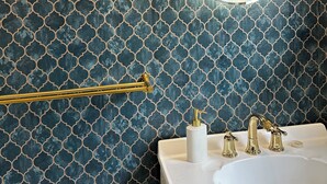 Une salle de bain avec un mur à motifs, un miroir rond, un porte-serviettes doré et un lavabo blanc doté de deux robinets.