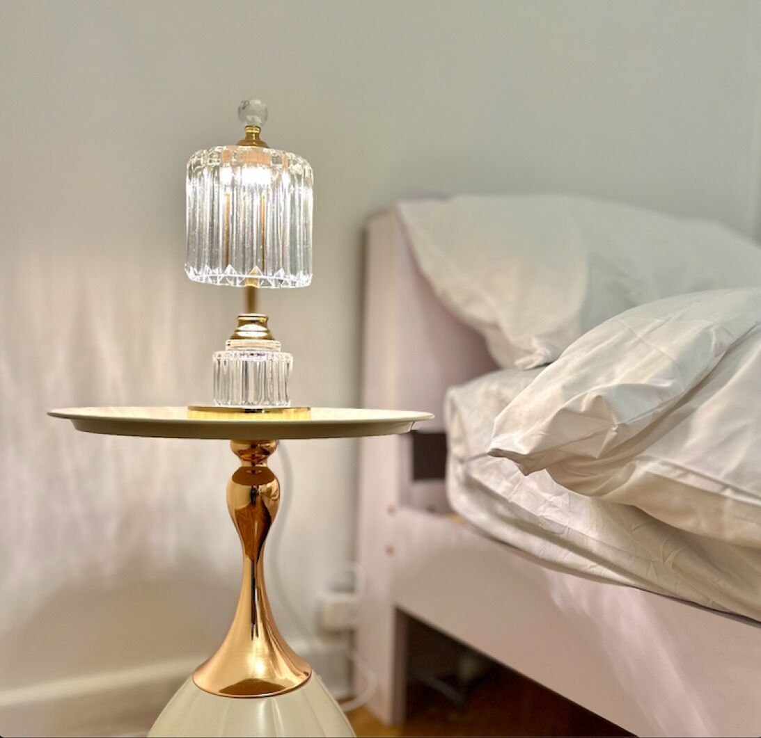 A bedside table with a crystal lamp and a white bed in the background.