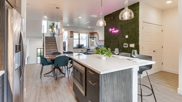 A modern kitchen with a central island, stainless steel appliances, and a green wall with a neon sign.