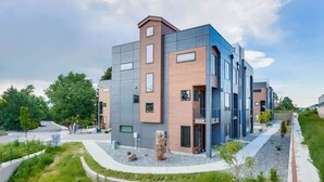 A modern multi-story building with a mix of glass and wood paneling, surrounded by a landscaped area with pathways and greenery.