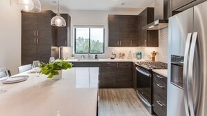 A modern kitchen with dark wood cabinets, stainless steel appliances, a central island, pendant lighting, and a window providing natural light.
