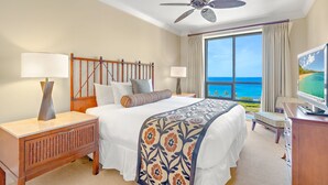 A hotel room with a bed, bedside tables, a TV, and a view of the ocean.
