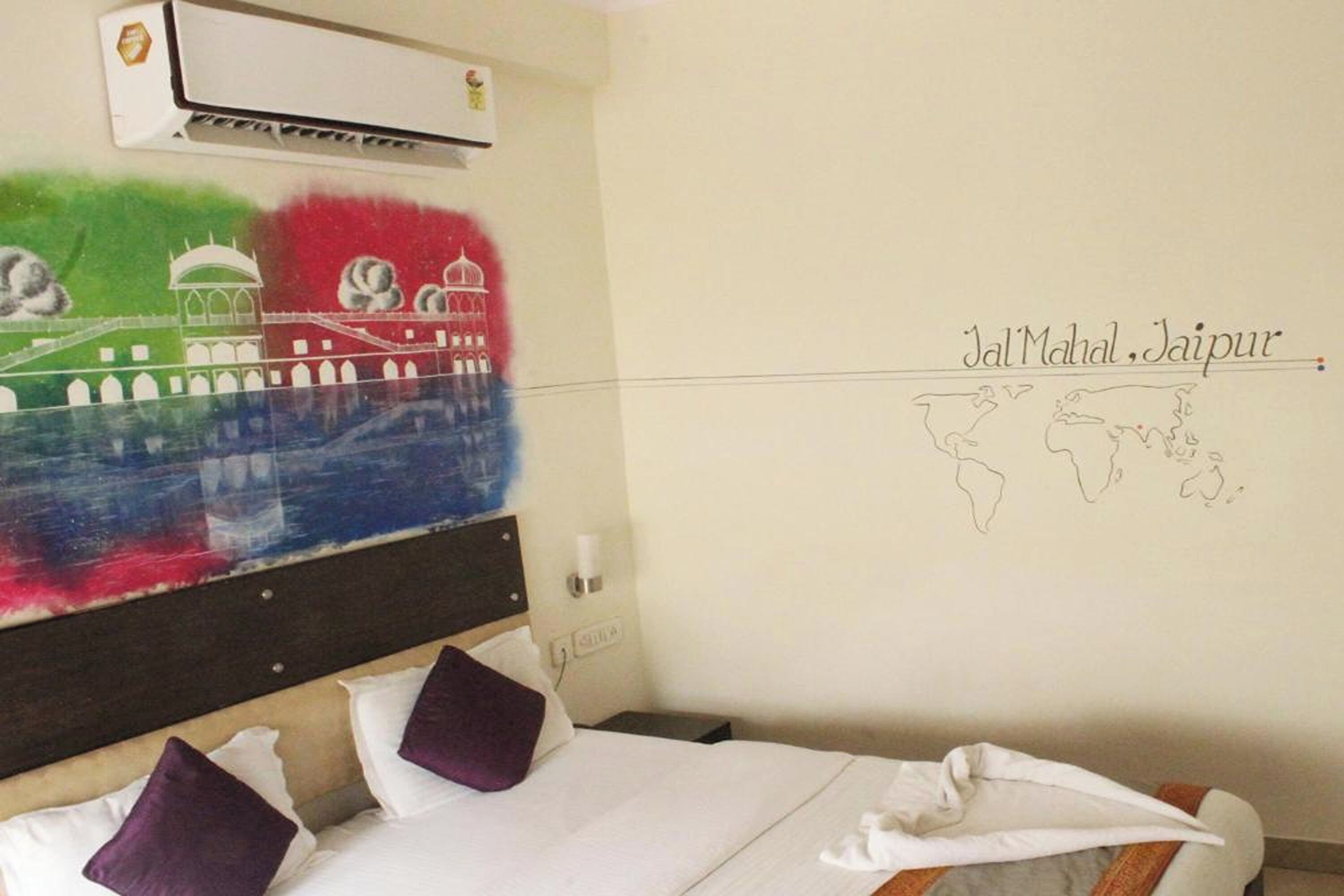 A hotel room with a bed, pillows, an air conditioner, and a wall with a mural and text.