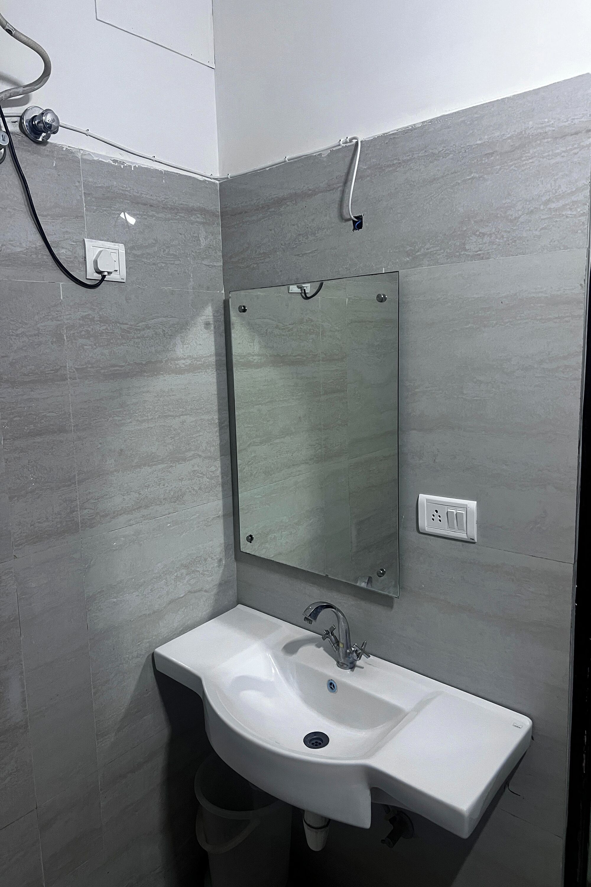 A bathroom with a white sink, a mirror, and grey tiled walls.