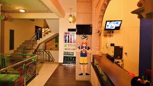 Eine Hotelhalle mit Treppe, einer Rezeption, einem Wand-Fernseher und einer ZoomCar-Werbung.
