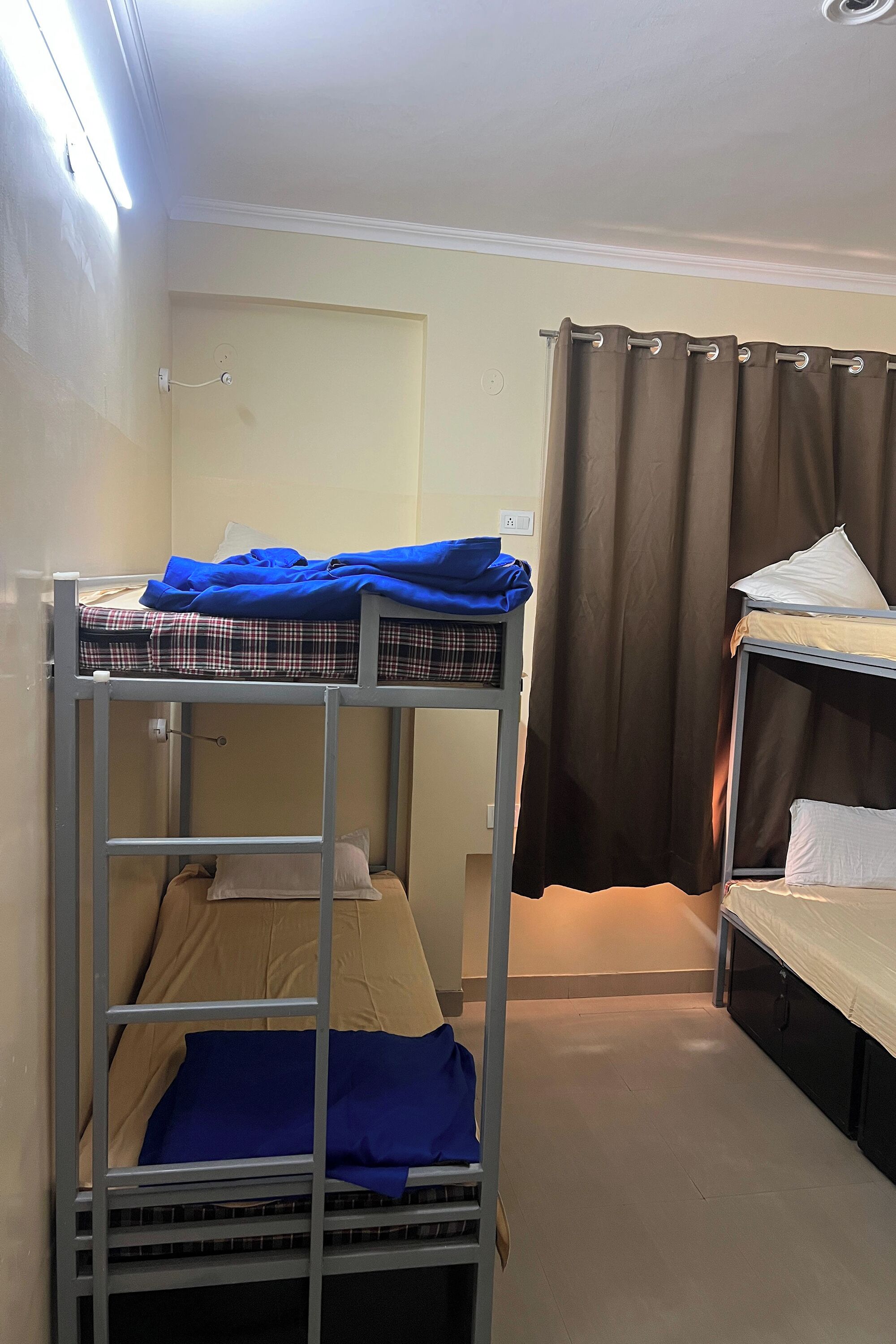 A dormitory room with bunk beds, a curtain, and a wall socket.