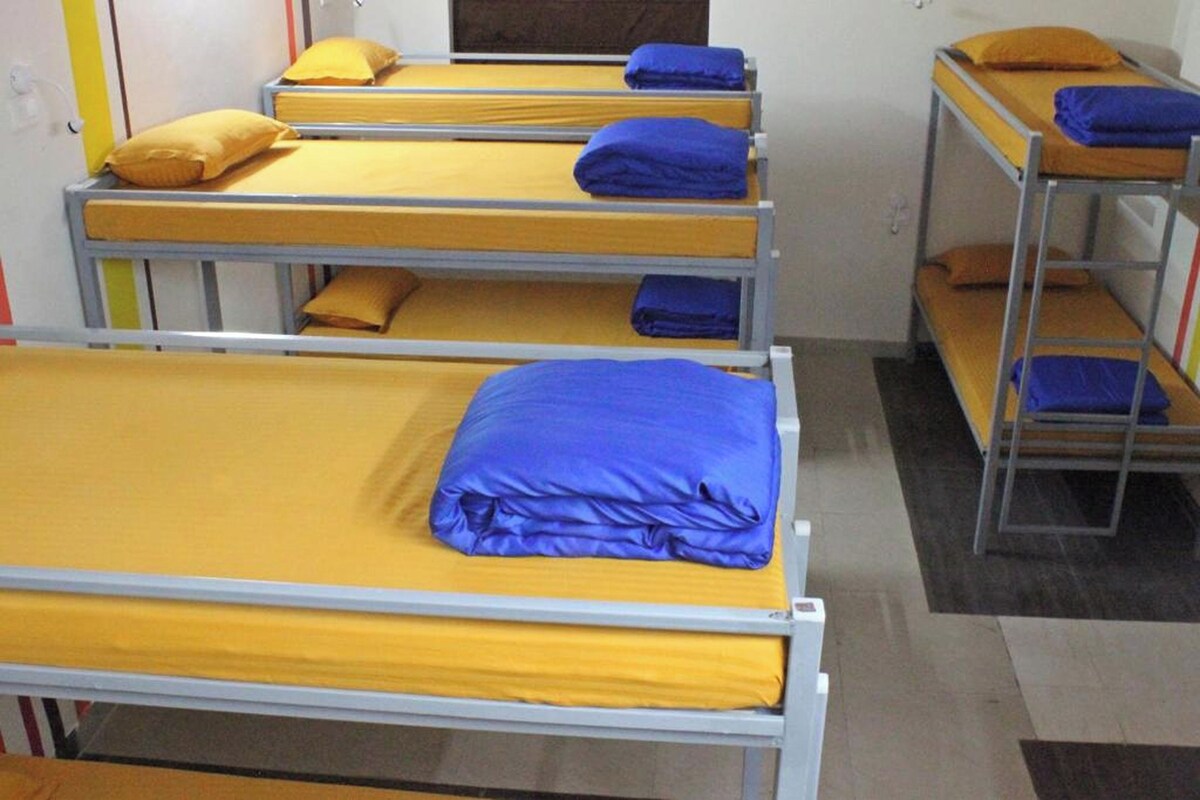 A dormitory room with bunk beds, each with a yellow mattress and blue pillows.