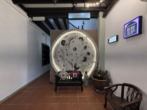 A hallway with a large moon-like sculpture, a bench, a potted plant, and a sign indicating a bakery. - Carnarvon Heritage Lodge (George Town)