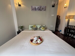 A neatly made bed with a tray of white cups and a teapot, a wall-mounted picture, and two wall sconces. - Carnarvon Heritage Lodge (George Town)