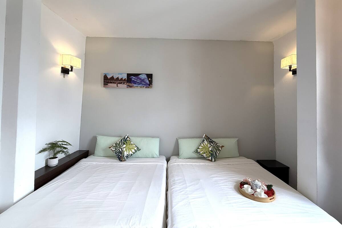 A twin room with two beds, a nightstand with a plant, a tray with breakfast items, and a picture on the wall.