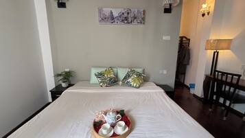 A neatly made bed with a tray of teaware and a painting above it.