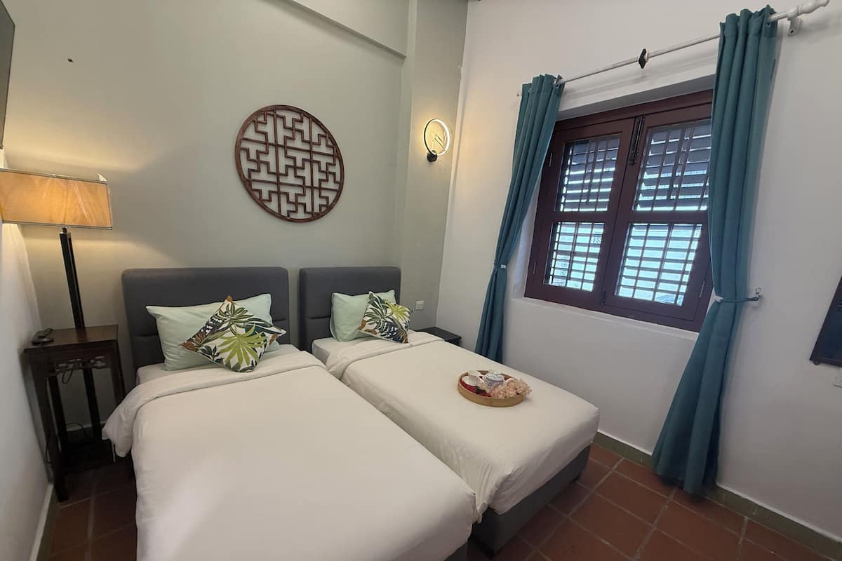 A room with two beds, a wall clock, a window with curtains, and a decorative wall piece.