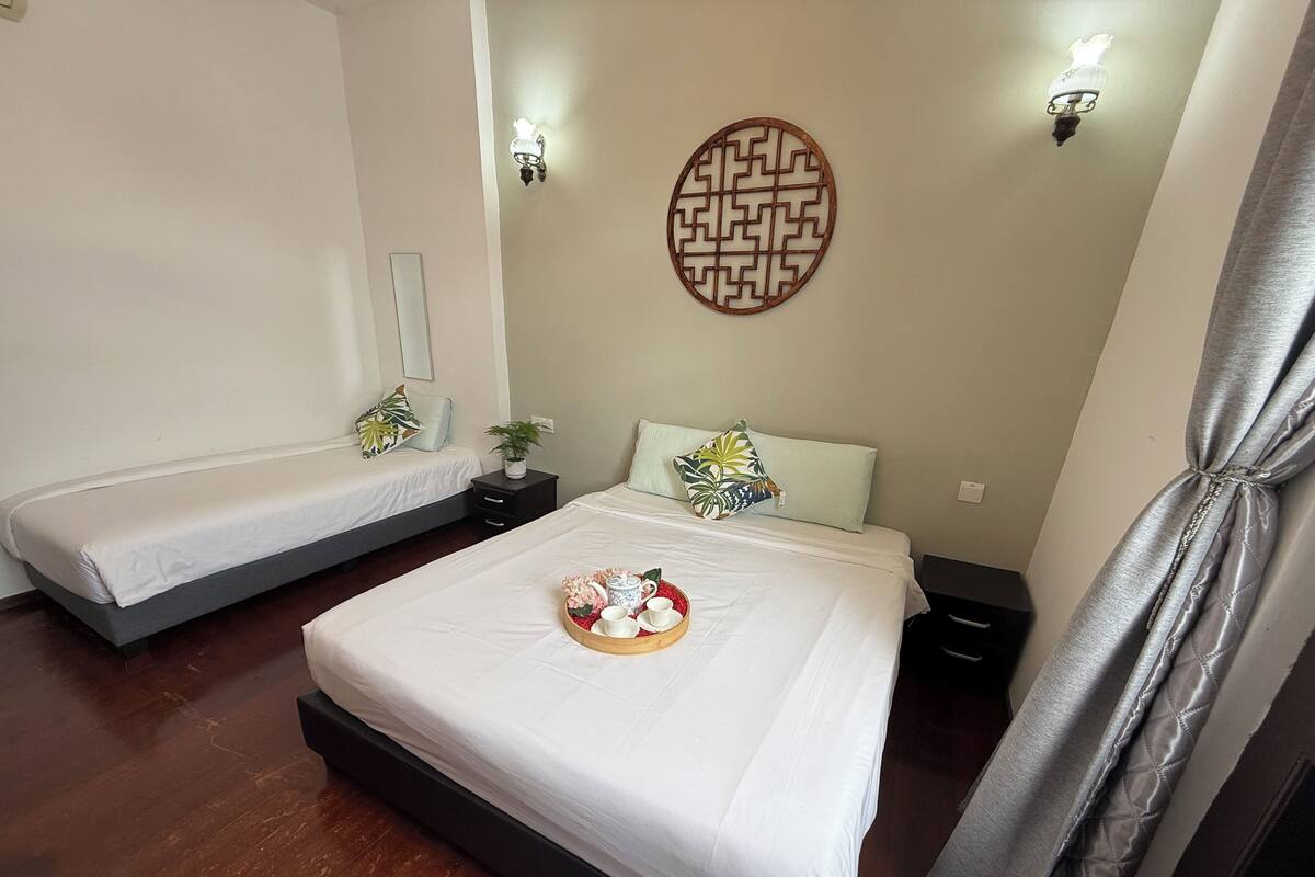 A hotel room with two single beds, a large bed with a tray of breakfast items, a decorative wall piece, and a ceiling light fixture.