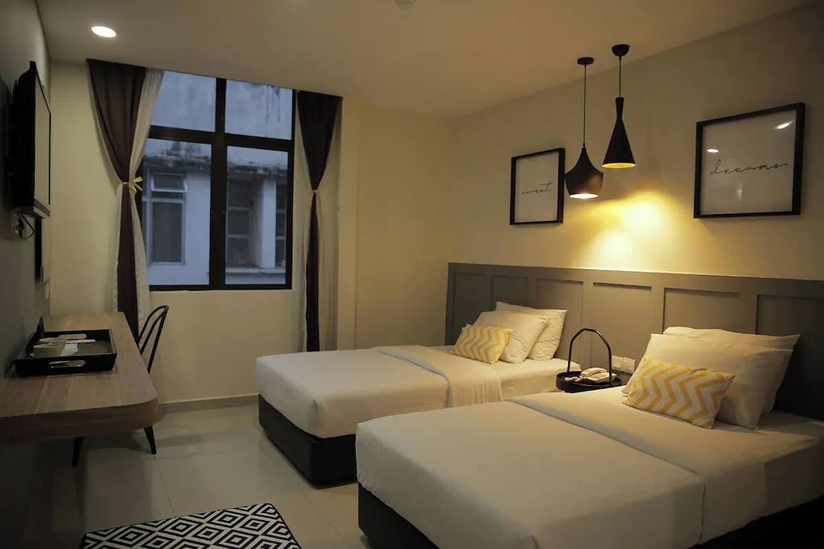 A hotel room with two beds, a desk, and a window with curtains.