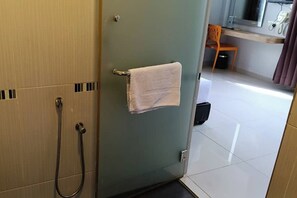 A bathroom with a towel hanging on the door, a shower, and a small desk with a chair. - Mars Hotel (Kuala Lumpur)