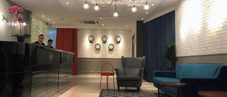 A reception area with a black reception desk, a chandelier, a blue sofa, and a patterned rug.
