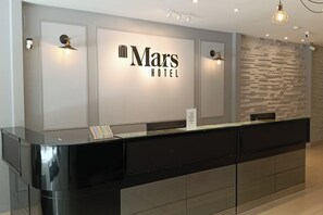 A reception desk with a Mars Hotel sign, a modern light fixture, and a textured wall. - Mars Hotel (Kuala Lumpur)