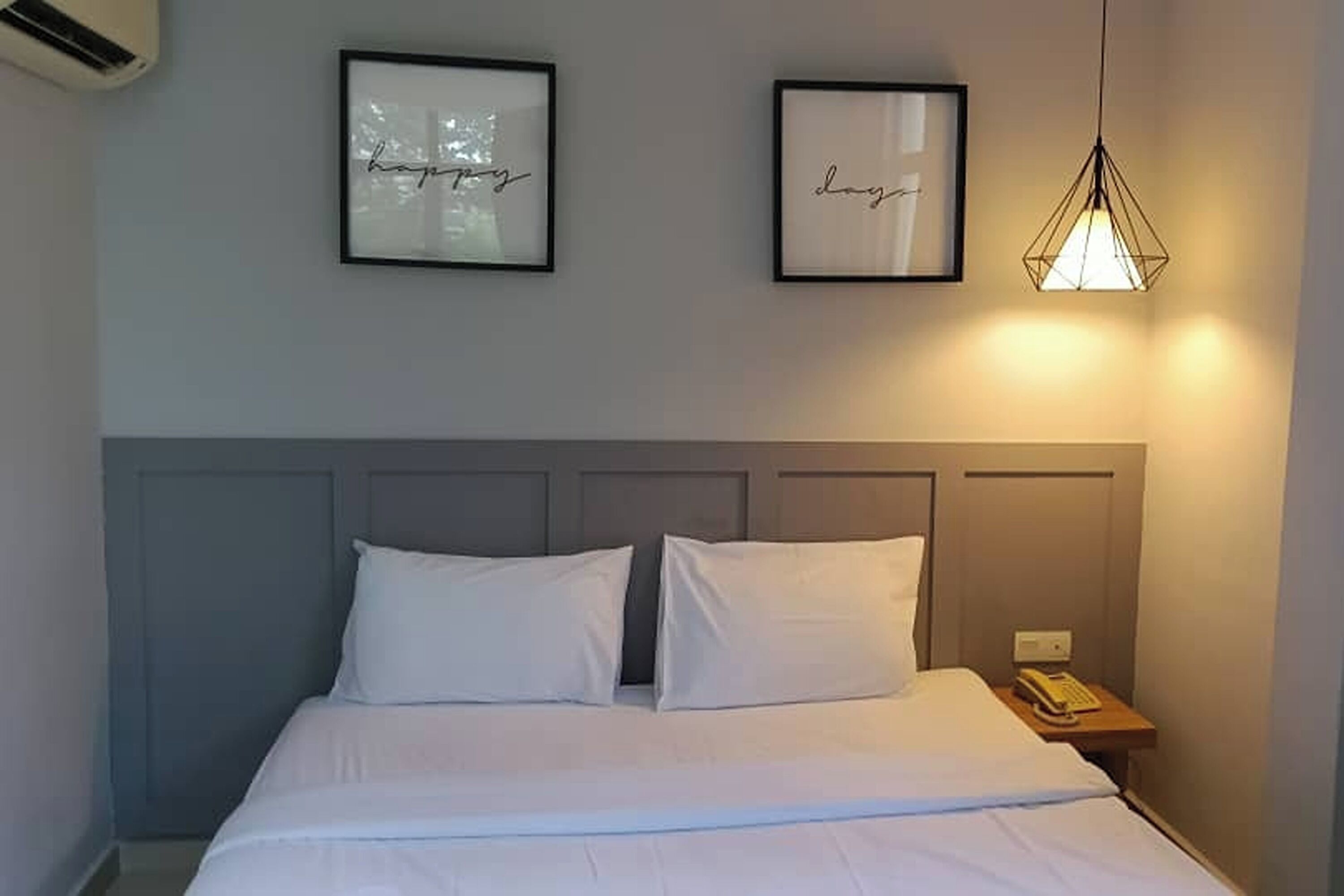 A neatly made bed with white bedding, a gray headboard, and two framed pictures on the wall.