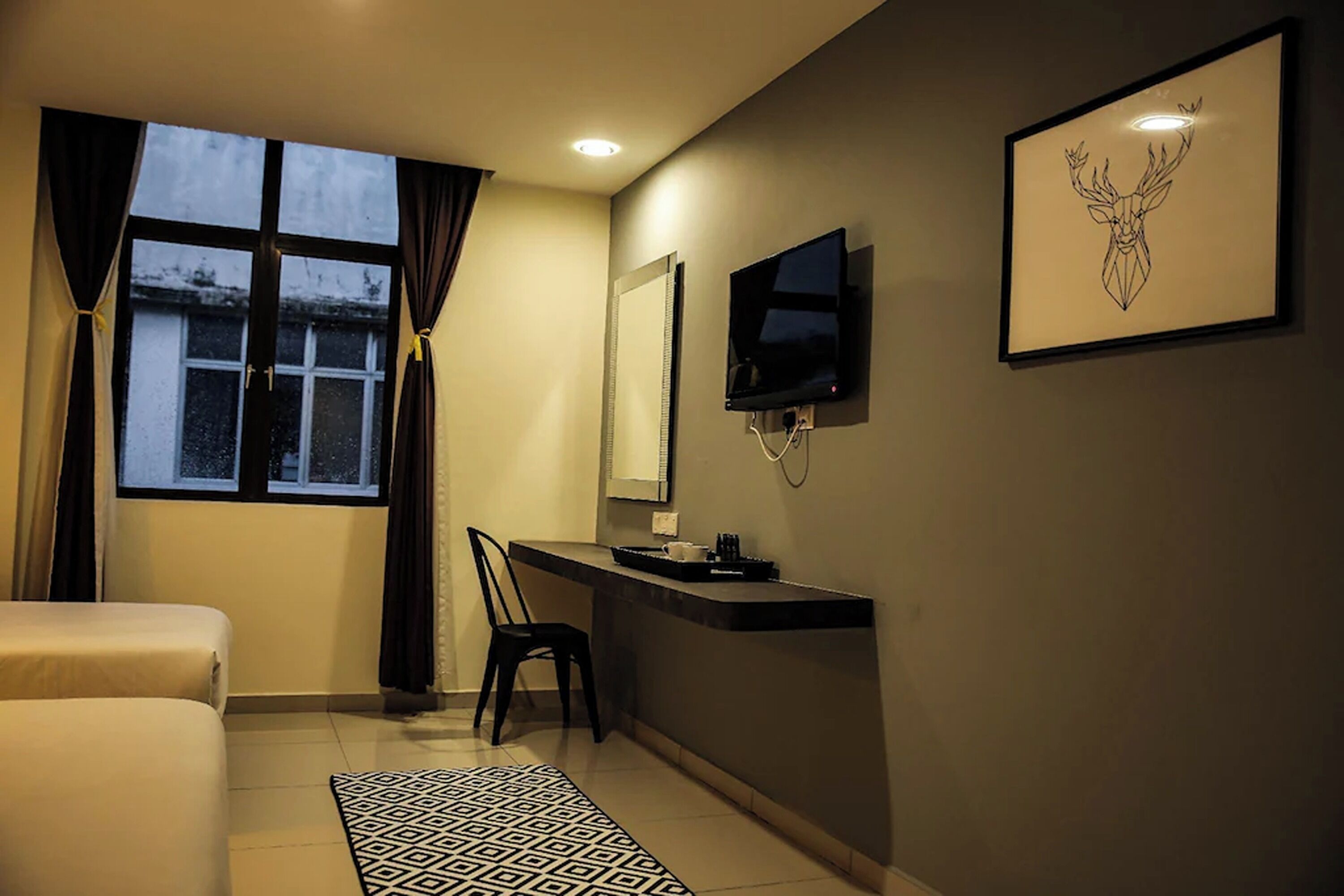 A modern hotel room with a bed, a desk, a chair, a TV, and a framed artwork on the wall.