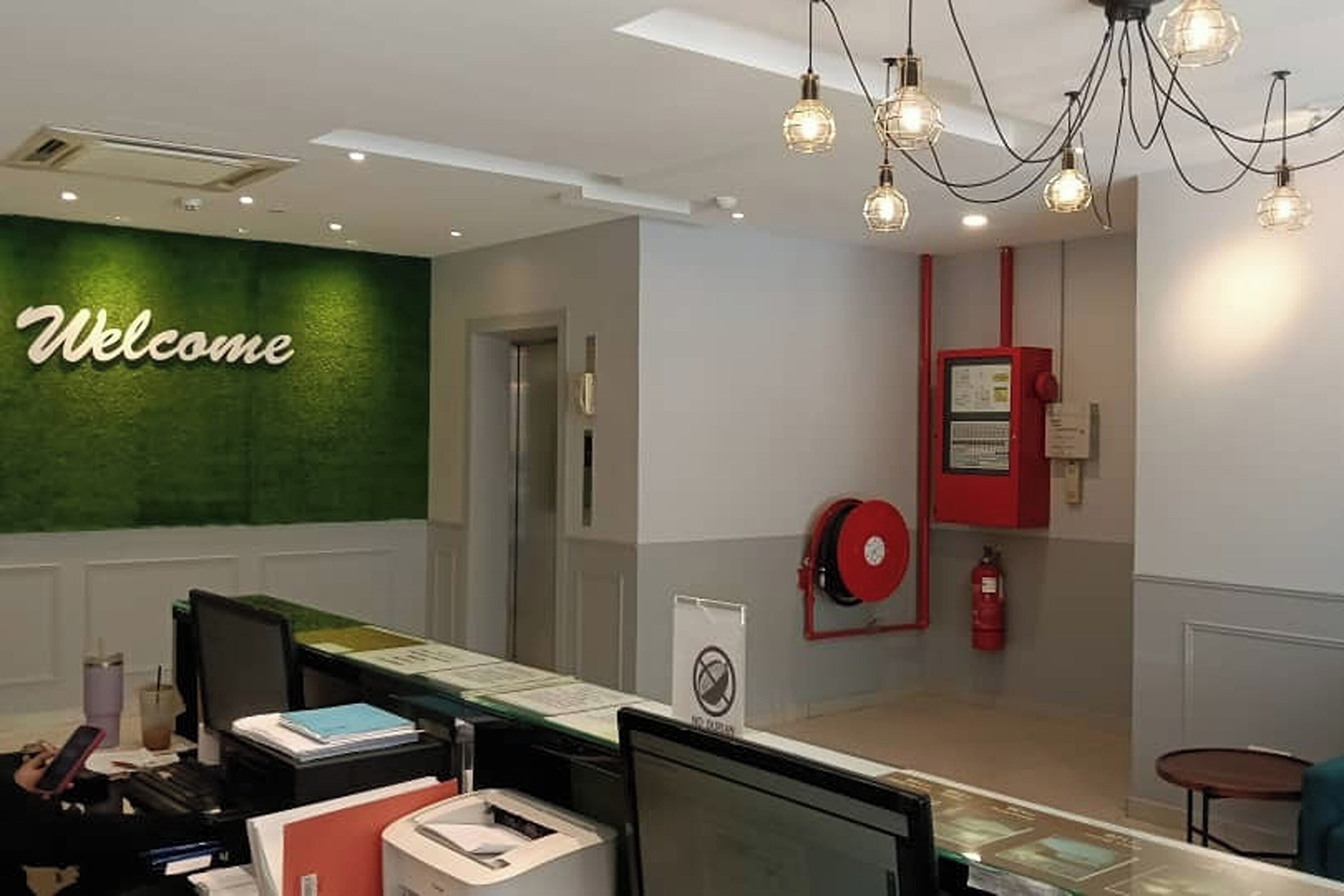 Uma área de recepção com uma placa de 'Welcome', um extintor de incêndio e um telefone vermelho de emergência.
