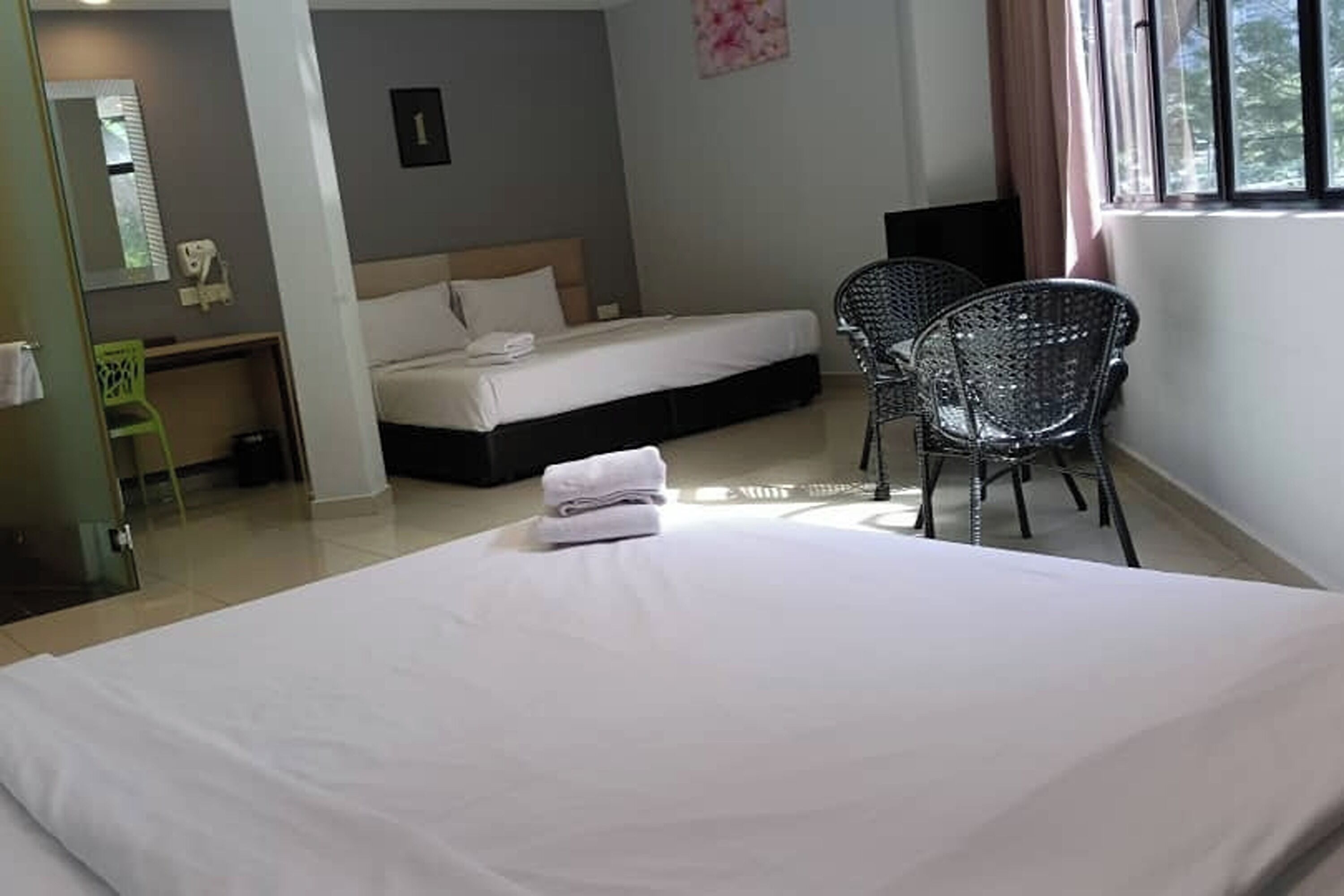 A hotel room with a large bed, a desk, two chairs, and a window with curtains.