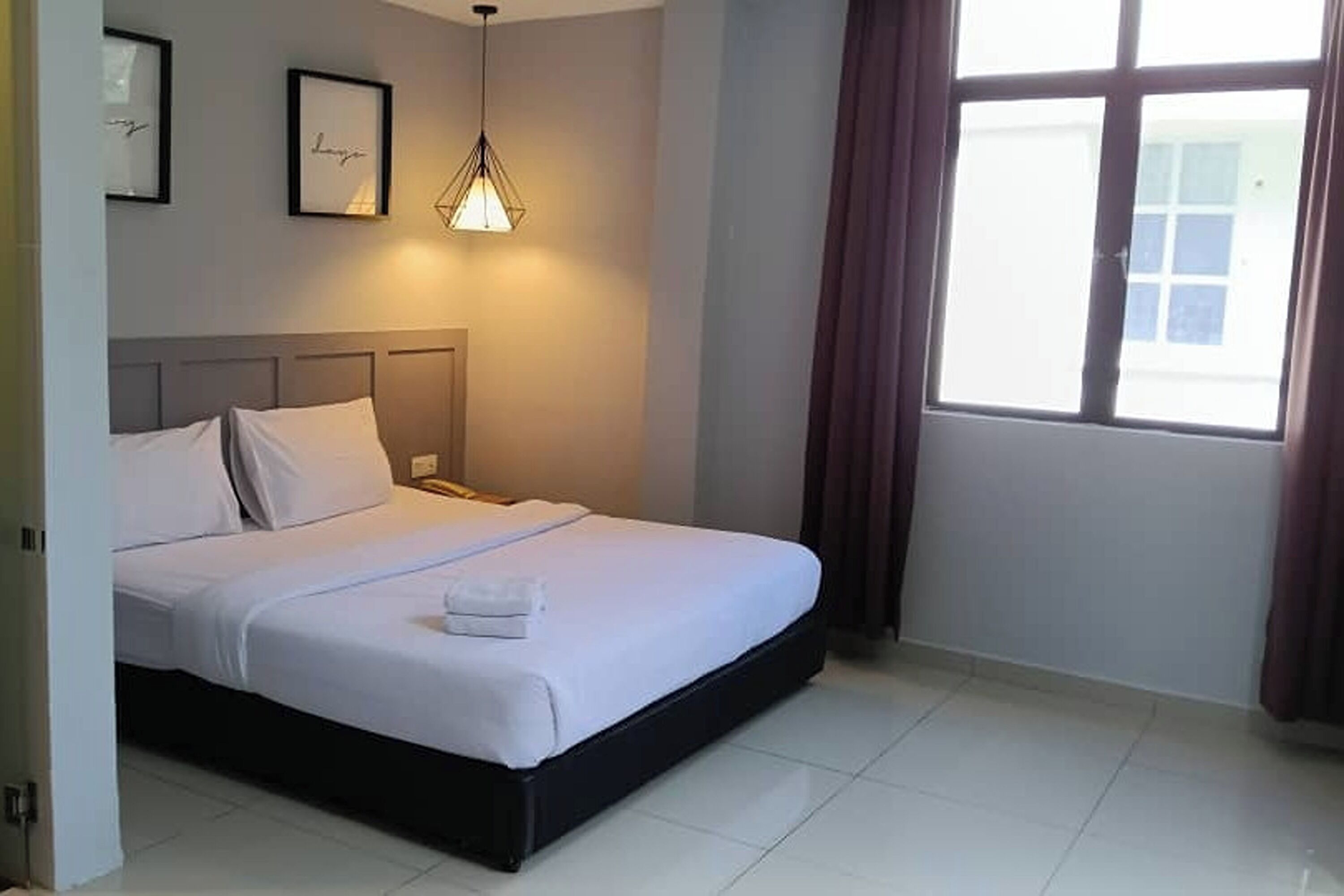 Una cama bien hecha en una habitación de hotel, con cabecera, mesita de noche y ventana con cortinas.