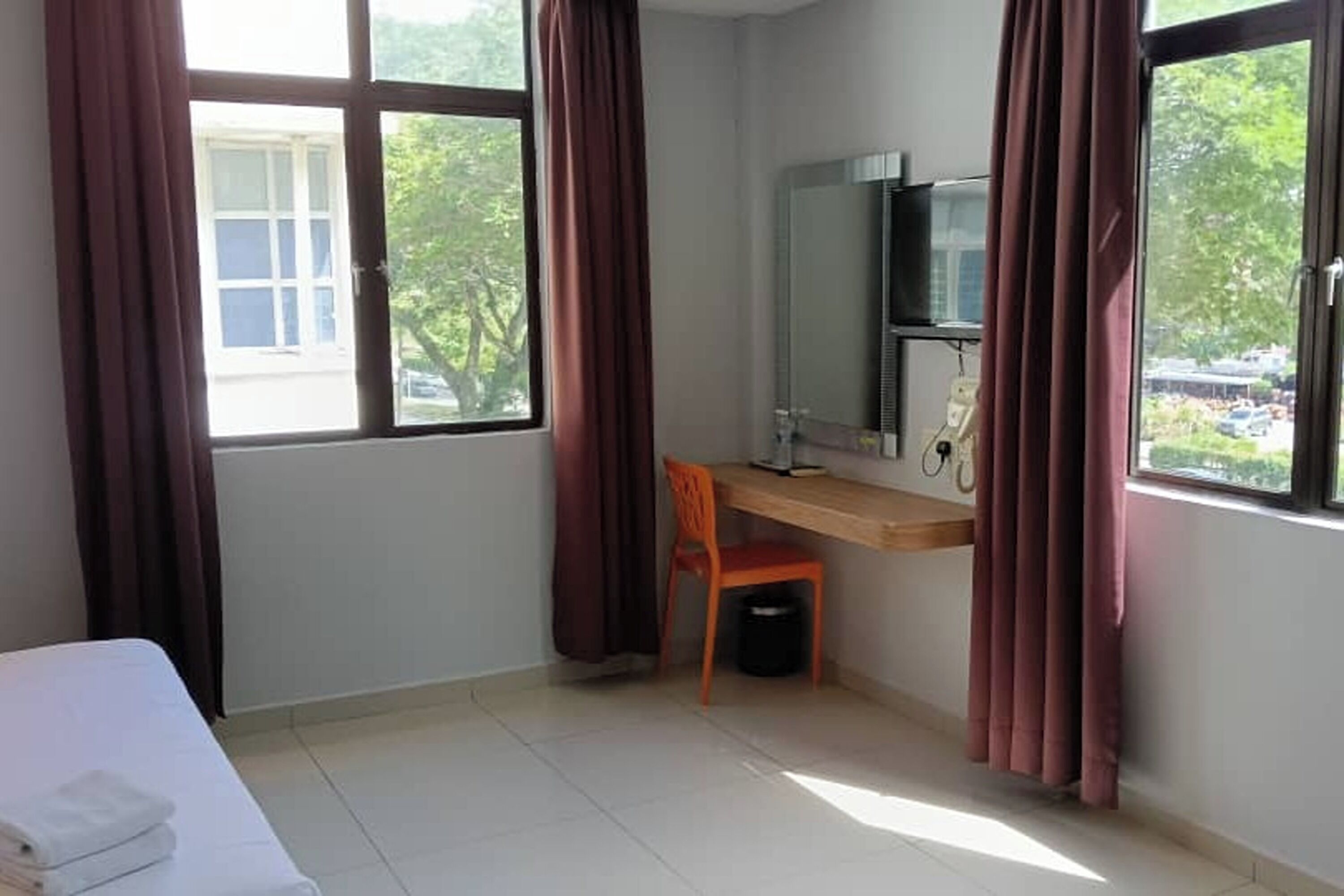 A hotel room with a bed, a desk, a chair, a mirror, and a window with curtains.