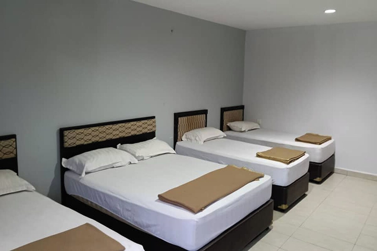 A hotel room with four single beds, each with a headboard and a brown blanket.