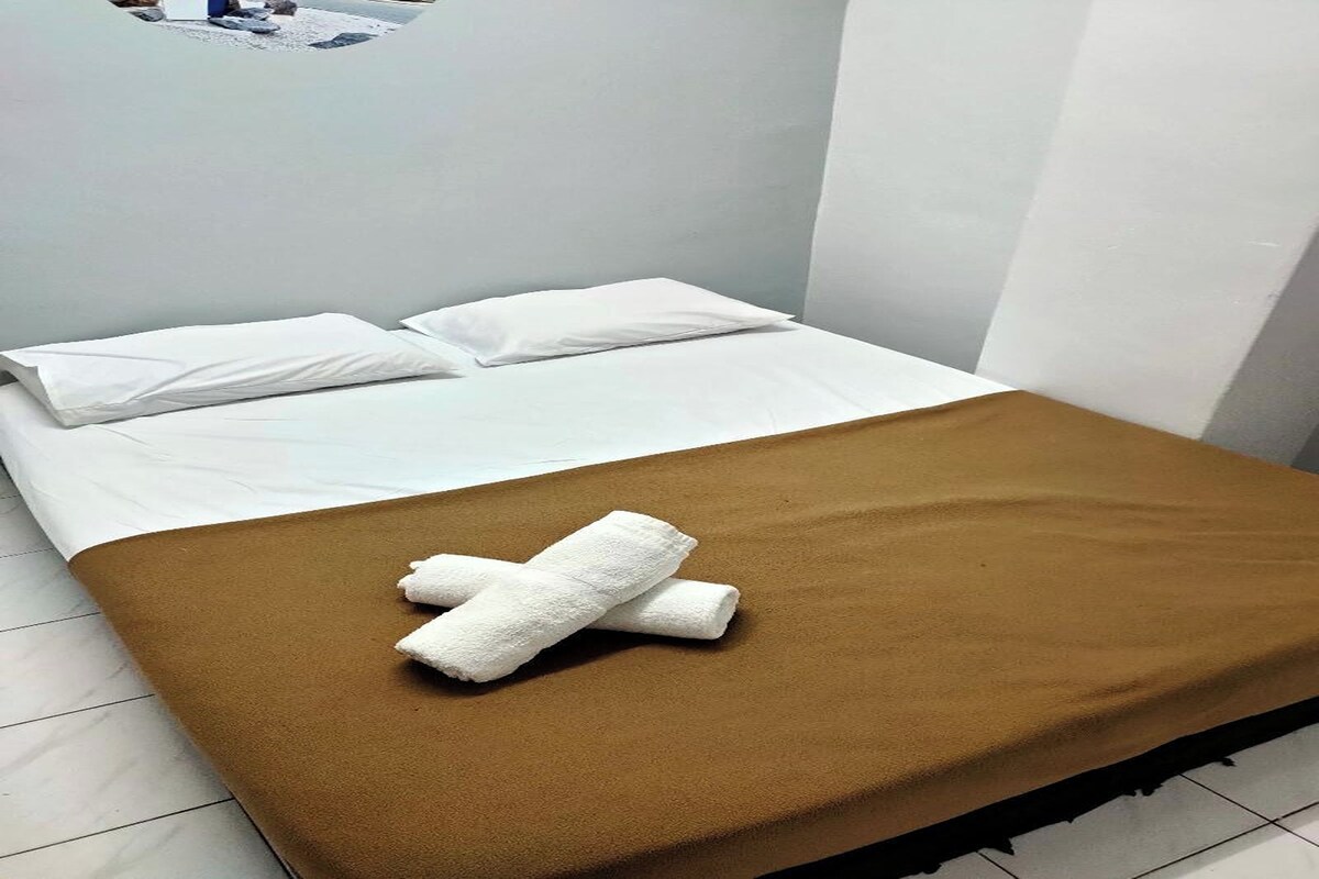 Un lit simple avec une literie blanche, une couverture marron et deux oreillers blancs.