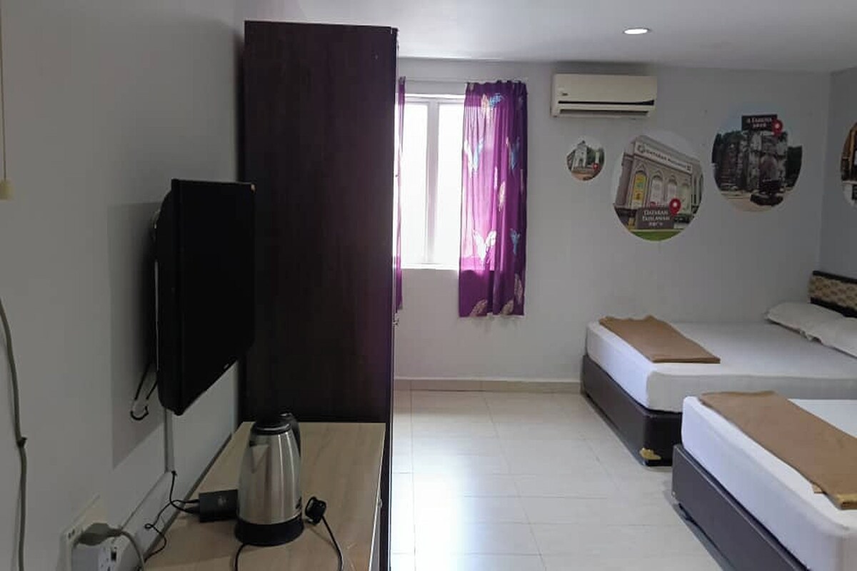 A room with a bed, a desk with a TV, a kettle, and a window with curtains.