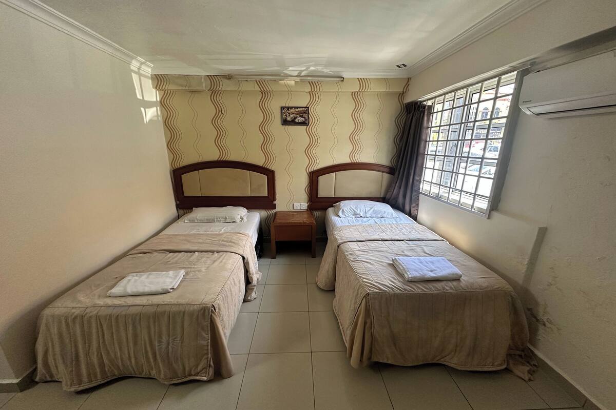 A room with two single beds, a small table, and a window with bars.