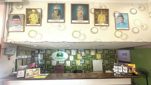 Zona de recepción de un hotel con retratos enmarcados en la pared, un reloj y varios certificados.