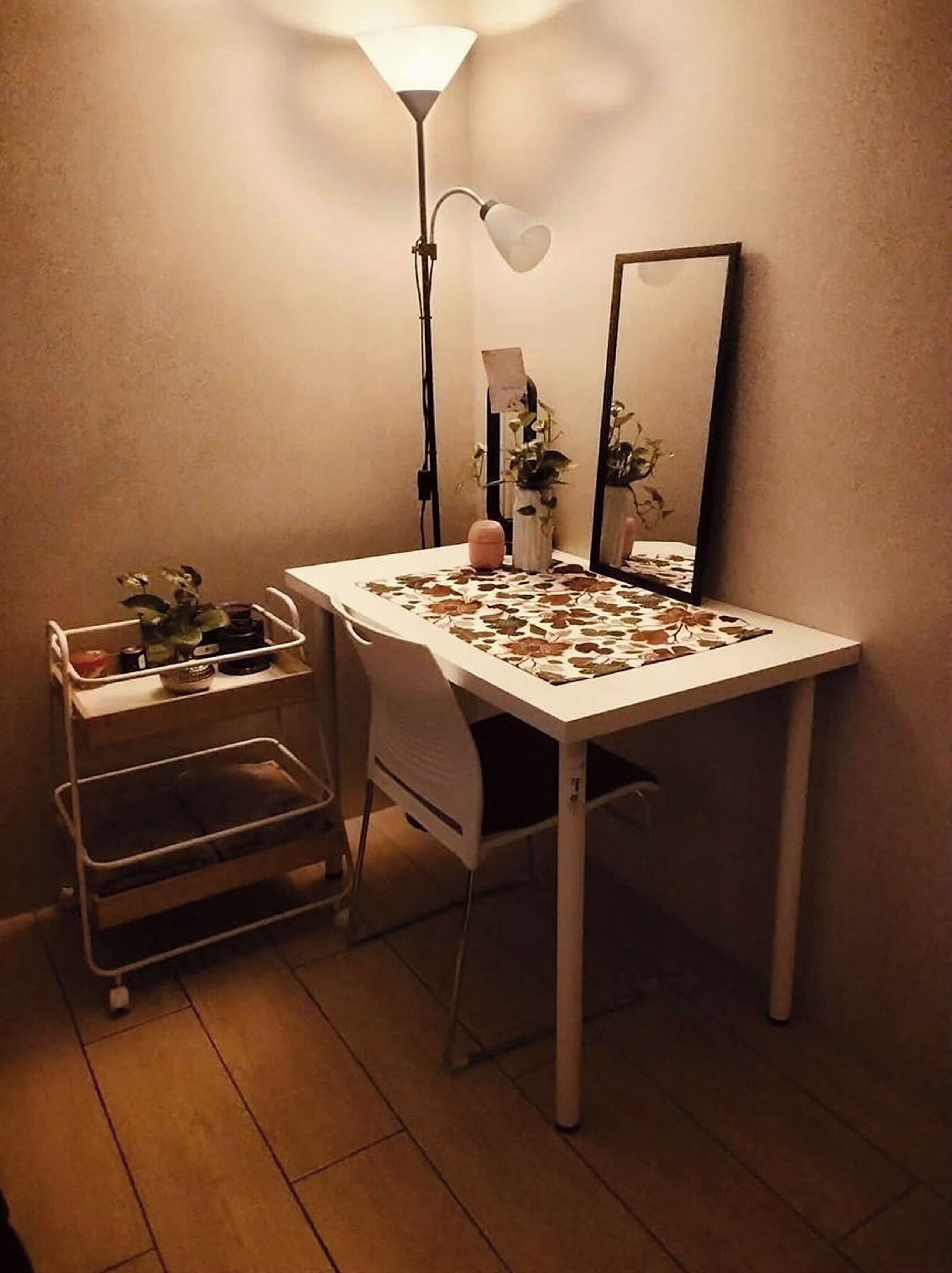 A small room with a white desk, a chair, a lamp, a mirror, and a plant.