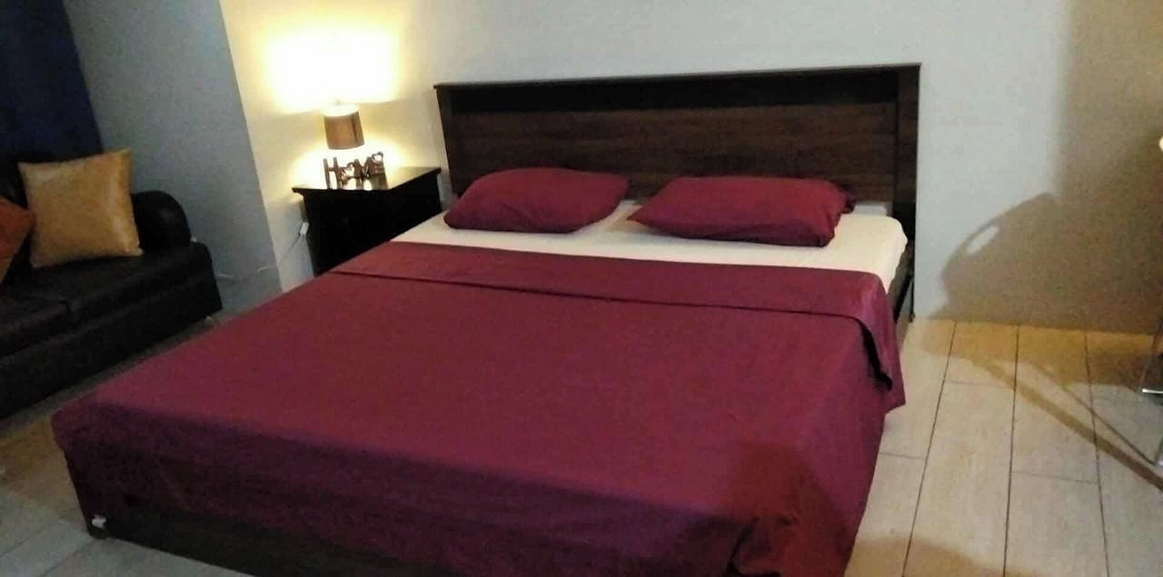 A bed with a dark headboard, two red pillows, and a red bedspread.