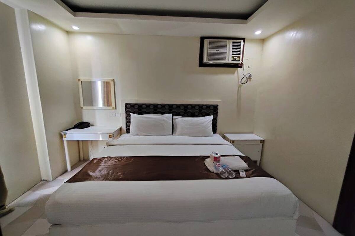 A hotel room with a bed, bedside tables, a mirror, and an air conditioning unit.