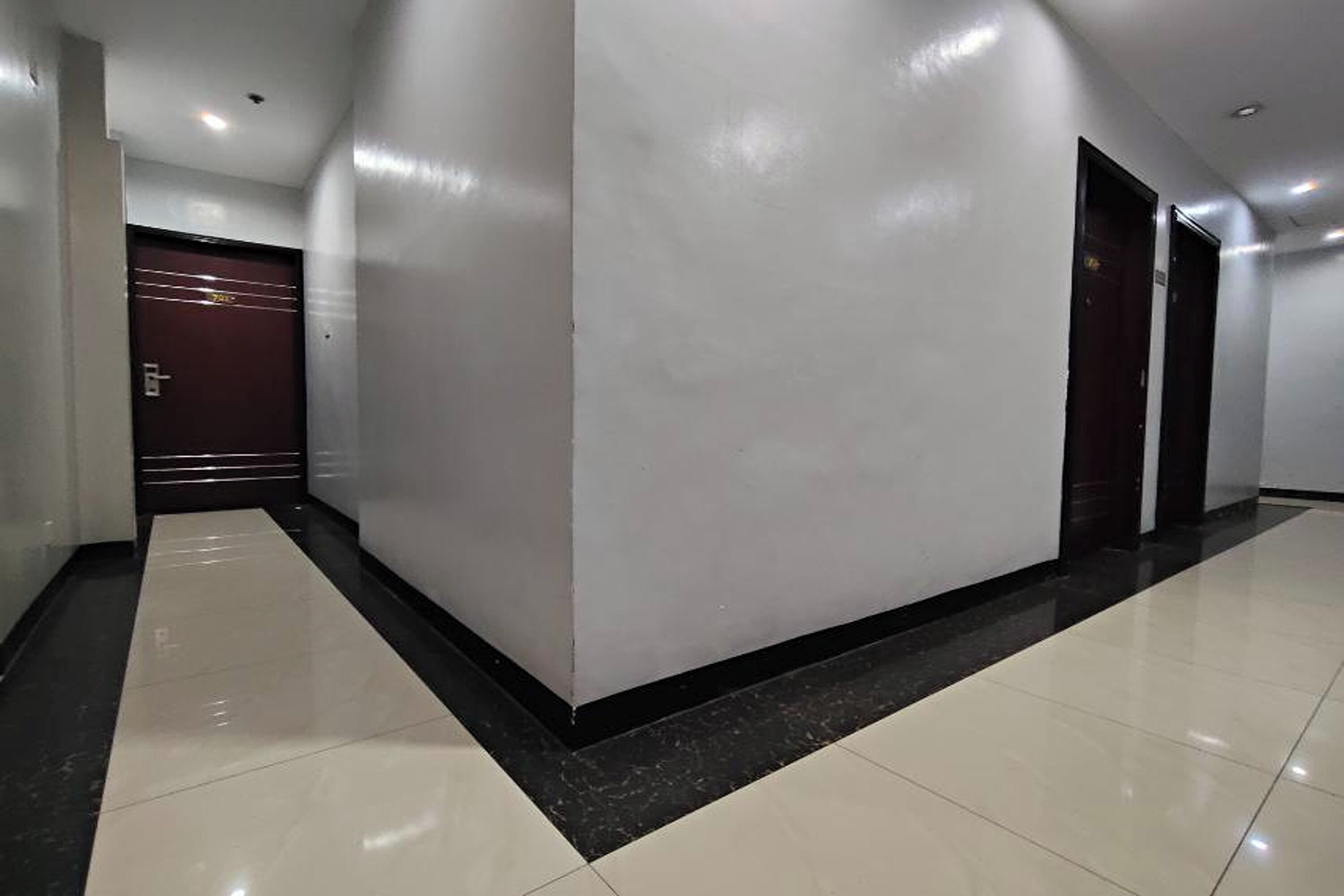 A corridor with a marble floor, white walls, and a dark door at the end.