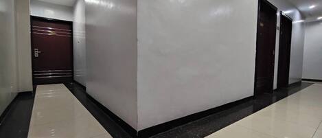 A corridor with a marble floor, white walls, and a dark door at the end.