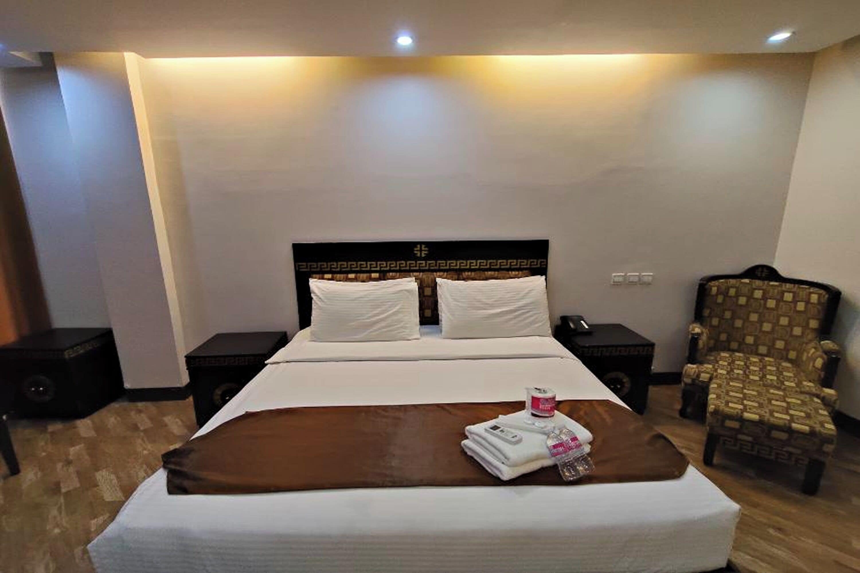 Una habitación de hotel con una cama grande, dos mesitas de noche, una silla y un televisor montado en la pared.