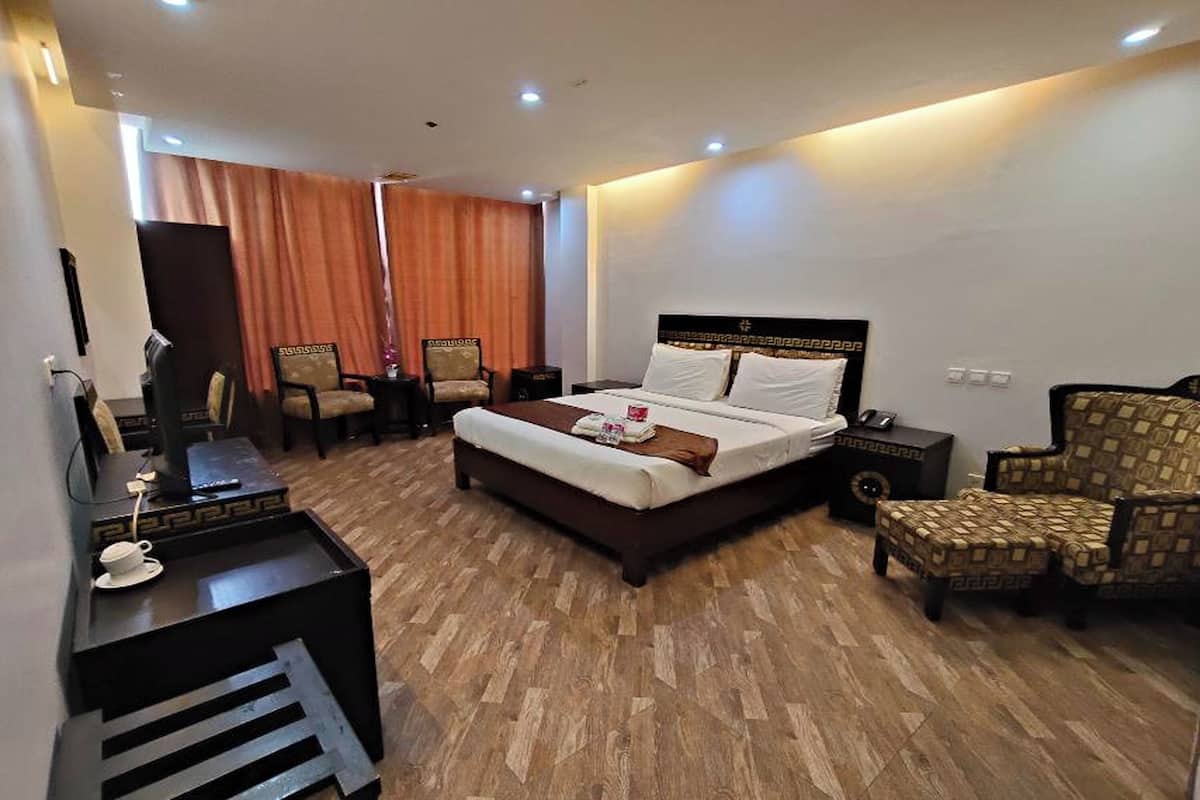 A hotel room with a large bed, two armchairs, a desk with a computer, and a coffee table.