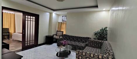 A living room with a sofa, a coffee table, and a TV. There is a door leading to another room.
